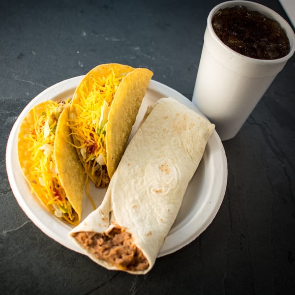 Three crispy tacos with cheese and a bean burrito on a plate, with a soda.