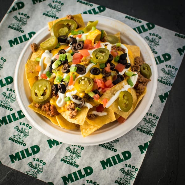 A plate of Taco Pronto nachos with cheese, ground beef, jalapeños, olives, tomatoes, and sour cream.