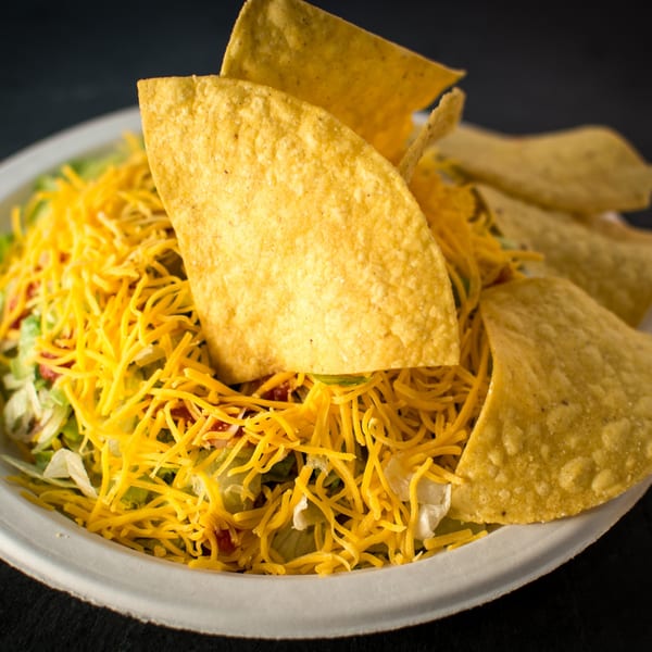Taco Pronto taco salad with shredded cheese, lettuce, and tortilla chips in a white bowl.