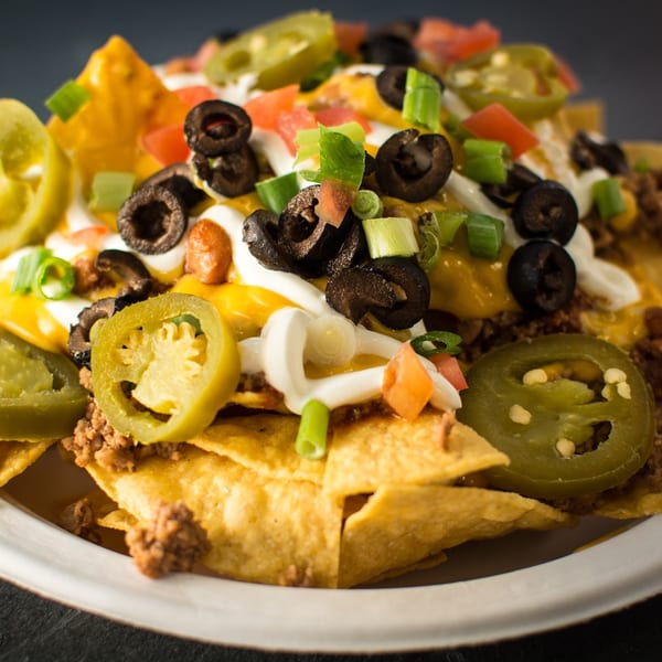 Close-up of Taco Pronto nachos with cheese, ground beef, jalapeños, olives, tomatoes, and sour cream.
