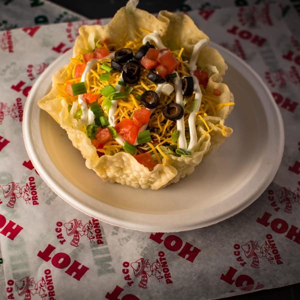 A Taco Pronto taco salad in a crispy shell, topped with cheese, olives, tomatoes, and sour cream.