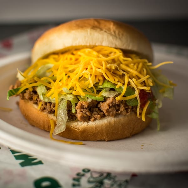 A Taco Pronto sloppy joe with ground beef, shredded lettuce, and cheddar cheese on a bun.